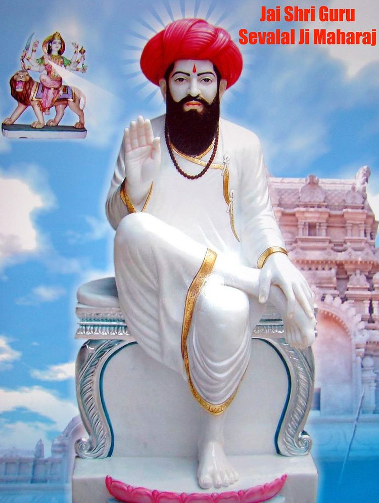 Poster of Sevalal sitting cross-legged, wearing a brown necklace, red turban, and a white robe.