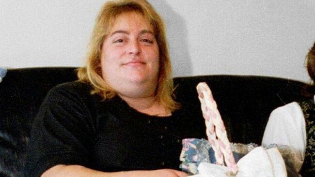 Sharon Lopatka with blonde hair, sitting on a black couch and wearing a black shirt.