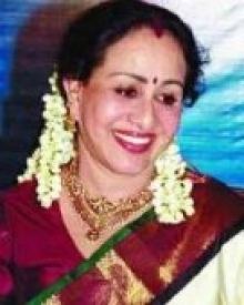 Sheela smiling while wearing a maroon blouse, green and maroon dupatta, gold necklace, earrings, and a gajra on her hair