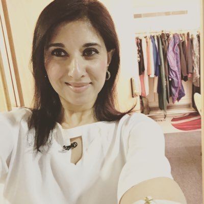 Shefali Oza taking a selfie while smiling at the dressing room and wearing a white blouse and earrings