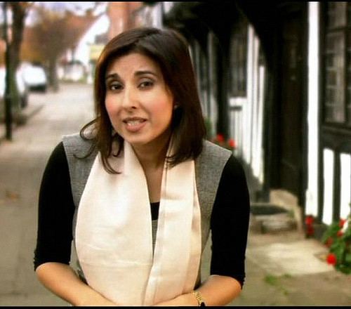 Shefali Oza speaking while wearing a black and gray blouse, cream scarf, and wristwatch