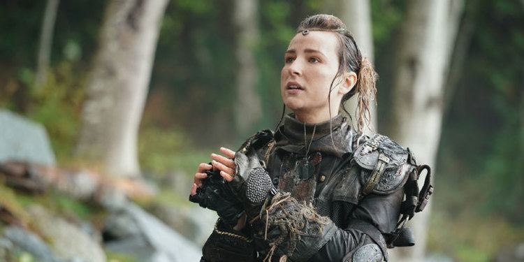 Shelby Flannery looking afar while wearing black long sleeves, gloves, and elbow pads in a scene from the 2014 television series, The 100
