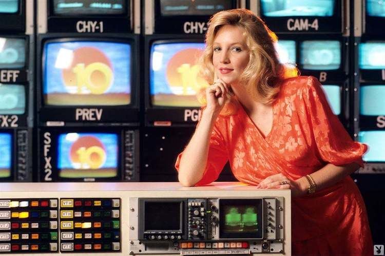 Shelly Jamison wearing an orange dress with monitors at the back