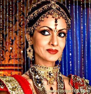 Shikha Swaroop smiling while wearing a red and gold traditional dress and headdress