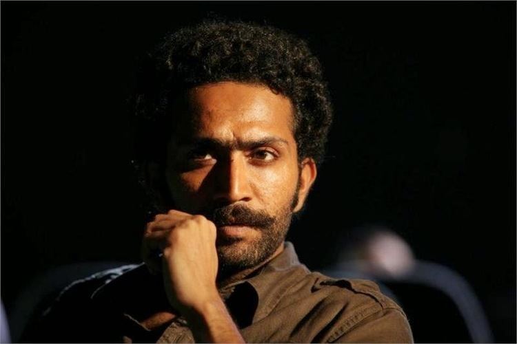 Shine Tom Chacko looking fierce with curly hair, right hand on mustache, beard and wearing a black shirt