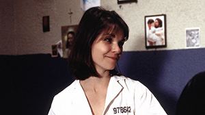 Shirley Bellinger with short hair and bangs smiling at someone and wearing her white inmate attire in a scene from Oz, 1997.