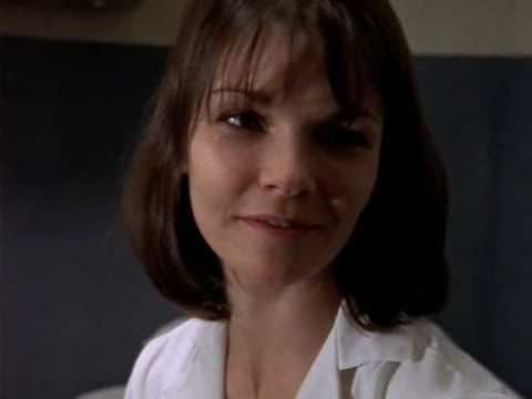 Shirley Bellinger with short hair and bangs smiling at someone and wearing her white inmate attire in a scene from Oz, 1997.