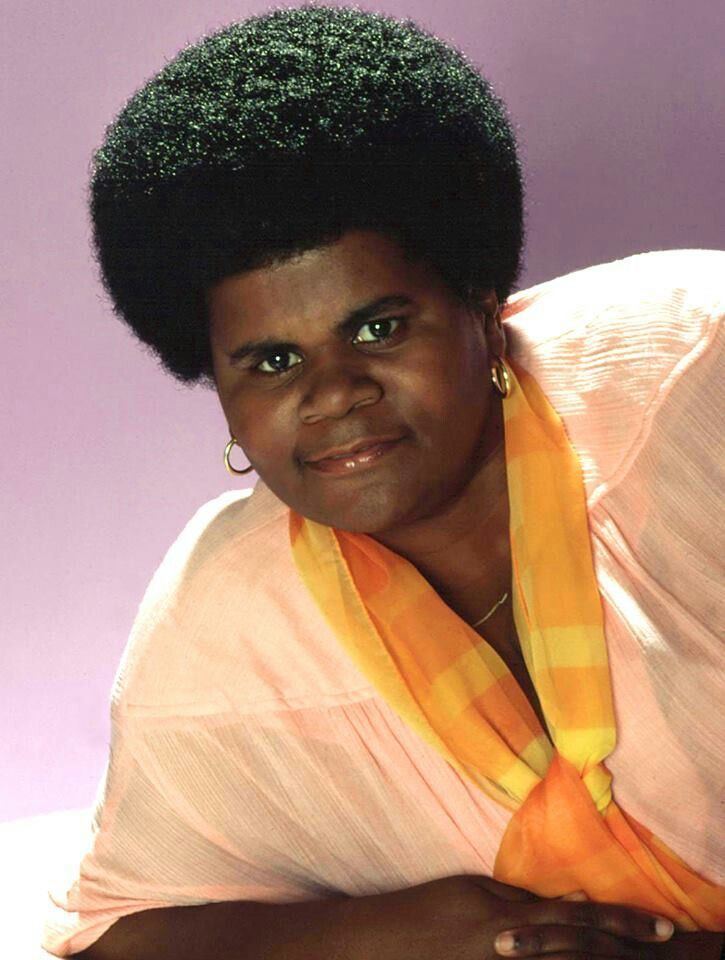 Shirley Hemphill wearing earrings, a necklace, a yellow scarf, and a light pink shirt.