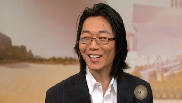 Sho Yano wearing eyeglasses, black coat and white long sleeves while smiling