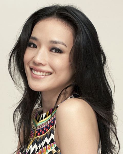 Shu Qi is smiling, has long black hair, and wears a geometrical design top with different colors.