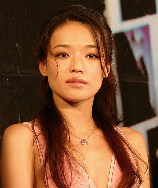 Shu Qi is serious, has long black hair, and wears a silver necklace, and a pink cleavage showing, sleeveless top.
