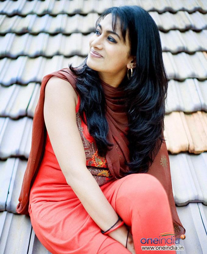 Shwetha Srivatsav smiling while looking afar, sitting on the roof, and wearing a brown dupatta, orange dress, and earrings