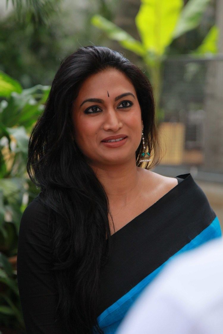 Shwetha Srivatsav talking to someone while wearing a black and blue blouse and earrings