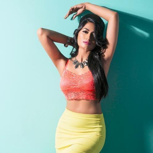 Shwetha Srivatsav with a fierce look while her arms up and wearing an orange lace top, yellow skirt, necklace, and bracelet
