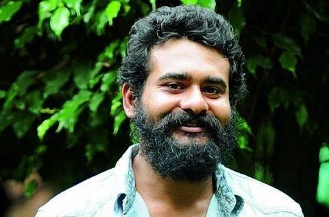 Sidharth Bharathan smiling with curly hair, mustache, and beard while wearing a light blue-green polo
