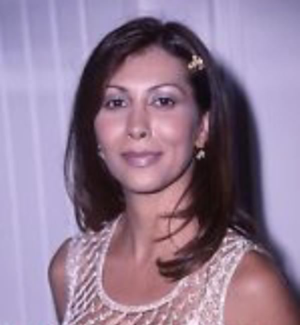 Sigal Erez smiling while wearing a white lace sleeveless blouse, clip on her hair, and earrings