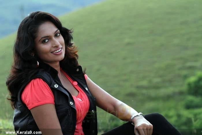 Rithi Mangal smiling while at the mountain and wearing a black vest, orange blouse, black pants, and bracelet