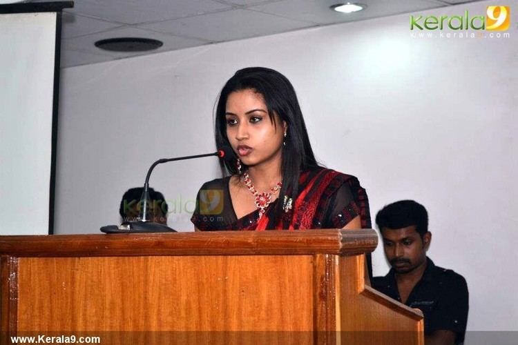 Agatha Magnus giving a speech while wearing a black dress, black and red dupatta, necklace, and earrings