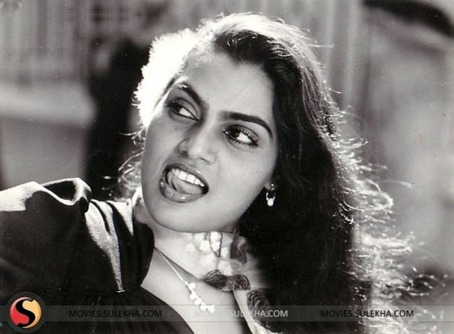 Silk Smitha looking at her side with a tongue out pose while wearing a blouse, scarf, necklace, and earrings