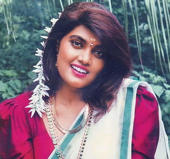 Silk Smitha smiling while wearing a red dress, white and green dupatta, necklace, and earrings