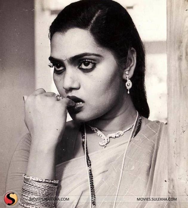 Silk Smitha looking afar while biting her finger and wearing a traditional Indian dress and some pieces of jewelry