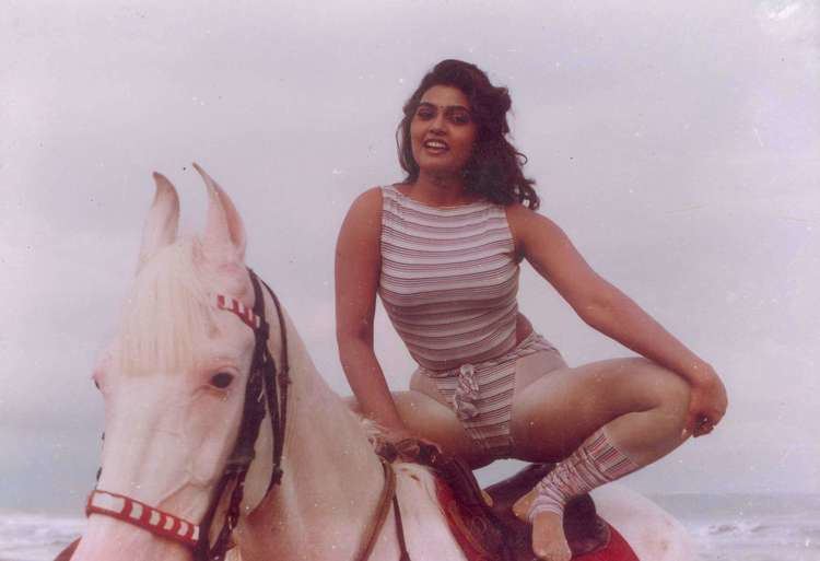 Silk Smitha smiling while riding on the horse and wearing a striped swimsuit