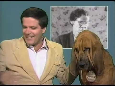 Simon Townsend smiling and wearing a brown suit with a dog beside him.