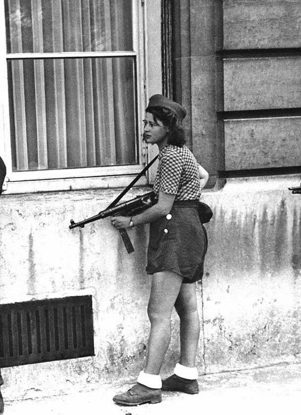 Simone Segouin holding a German MP 40 during the liberation of Paris while wearing a blouse, shorts, hat, and shoes