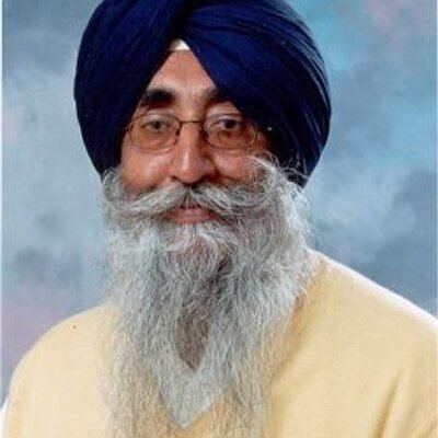 Simranjit Singh looking serious with a beard and a mustache, wearing a beige color shirt, eyeglasses, and blue turban
