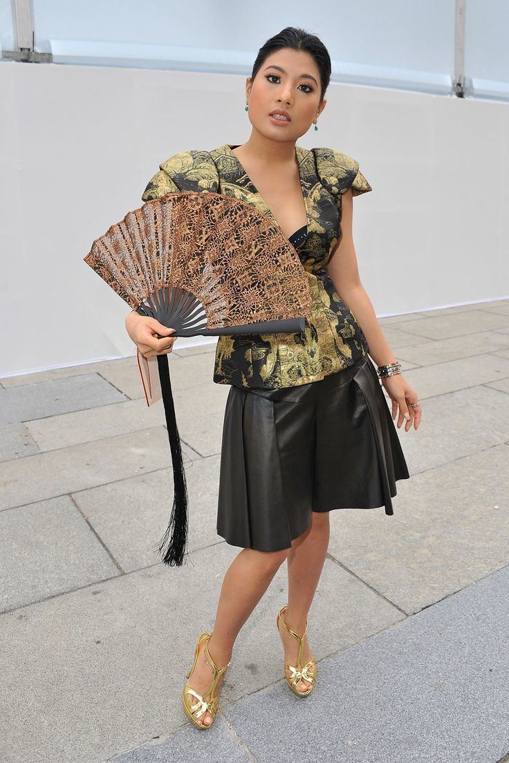 Sirivannavari Nariratana posing while holding a brown hand fan and wearing a gold and black blouse, black skirt, gold heels, and bracelet