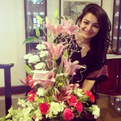 Sitara Suresh smiling behind a bouquet of flowers having a card in it with her long hair down and wearing a black dress