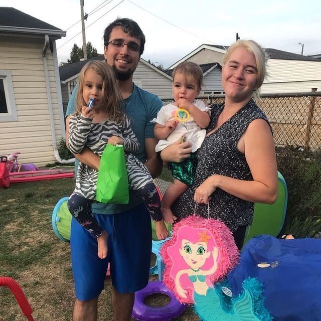 SmellyOctopus smiling with his wife Kelly while carrying their two daughters, Penelope and Zelda. SmellyOctopus wearing eyeglasses and a green shirt while his wife wearing a sleeveless black and white top.