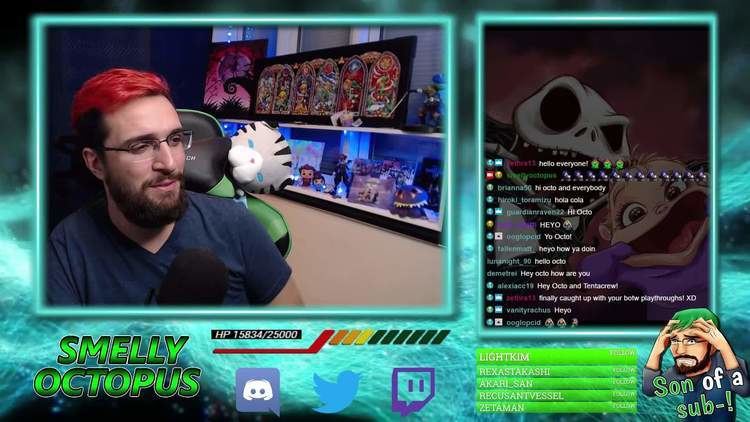 SmellyOctopus smiling and sitting on a gaming chair while streaming on Twitch channel, with beard and mustache, with red hair, wearing eyeglasses, and blue shirt.