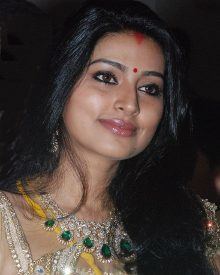 Sneha with a tight-lipped smile and looking afar while wearing an emerald necklace