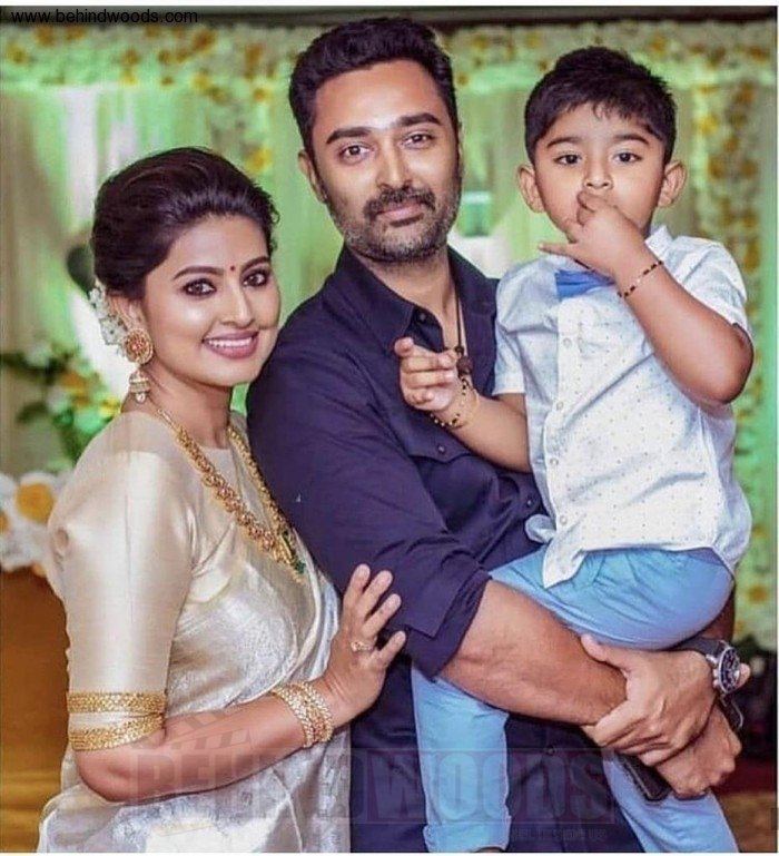 Sneha smiling and wearing a cream and gold dress and some jewelry while Prasanna carrying their son and wearing blue long sleeves