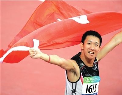 So Wa Wai smiling while holding the Hong Kong flag and wearing a black and white jersey with the number 1615