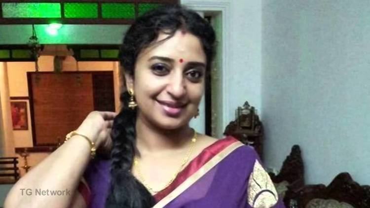 Sona Nair smiling, wearing earrings, a necklace, a bracelet, and a colorful dress.