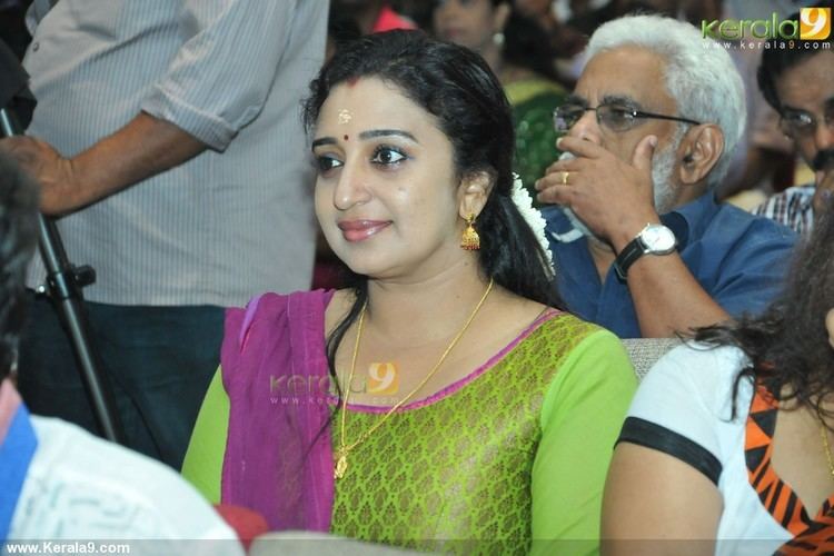 Sona Nair smiling, wearing earrings, a necklace, and a green dress with a purple scarf.