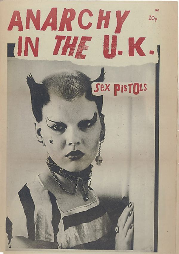 On a poster of Anarchy in the UK (Sex Pistols), Soo Catwoman is serious while standing, while both hands on the wall, has spiky black hair and gray in the middle, funky makeup and nail polish, a star on her right cheek, wearing skull earrings on her left ear and horn earing on right with a chain with bell on black choker, black and white striped shirt.