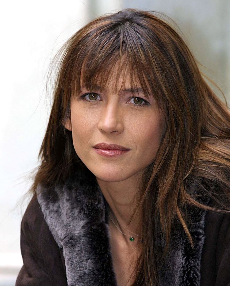 Sophie Marceau smiling with her hair down and wearing a coat