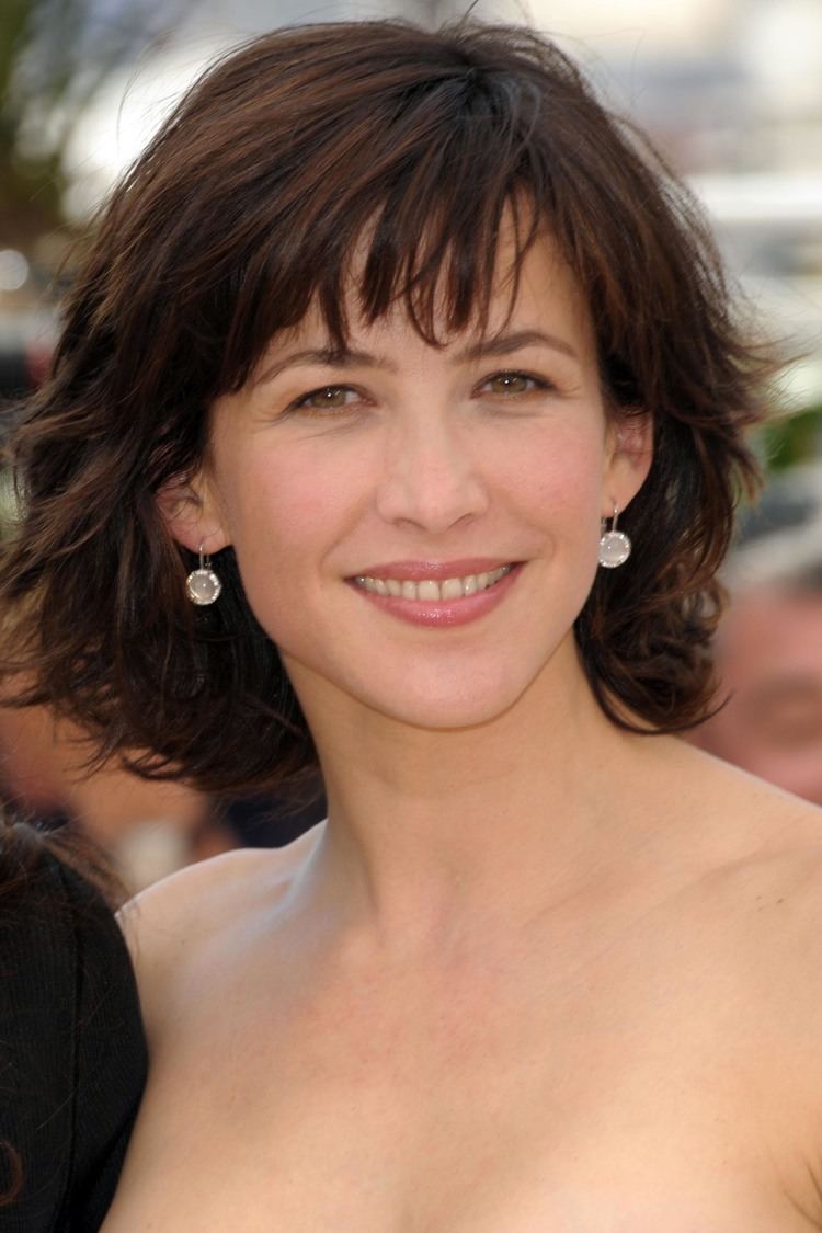 Sophie Marceau smiling with a short hair and earrings
