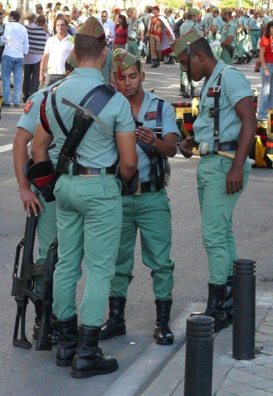 Group of Legionnaires looking at something while wearing the sage-green army uniform, black boots, and the chapiri sidecap