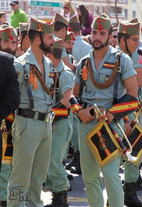 Legionnaires holding trumpets while wearing the sage-green army uniform, black boots, and the chapiri sidecap