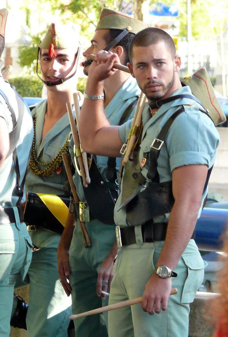 Legionnaires holding drumsticks while wearing the sage-green army uniform, black boots, and the chapiri sidecap