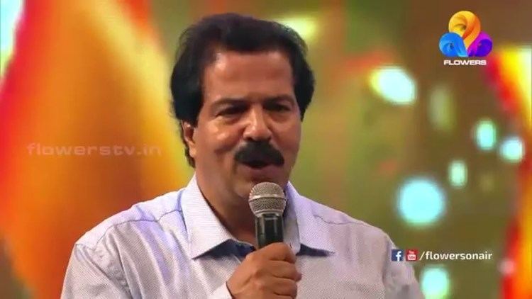 Sreekandan Nair speaking while holding the microphone and wearing white long sleeves