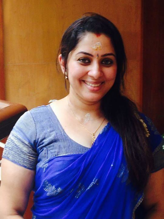 Sreeya Remesh smiling with a bindi on her forehead and tika on forehead & neck, she has vermilion in her black hair wearing earrings, a necklace, and a blue saree