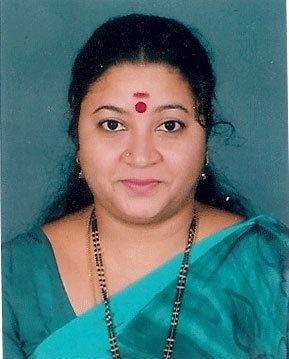 Sri Lakshmi smiling with a red mark on her forehead and nose pierceing while wearing a blue saree, beaded necklace and earrings