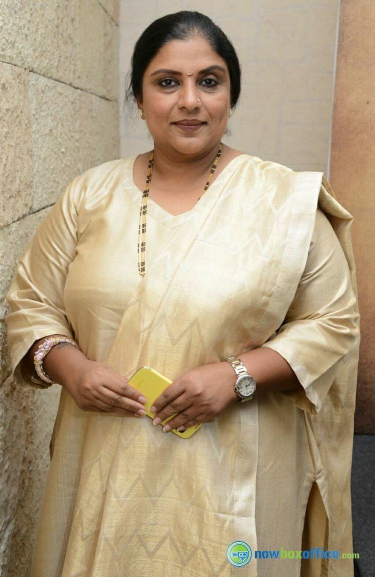 Sripriya wearing a gold dress while holding her phone