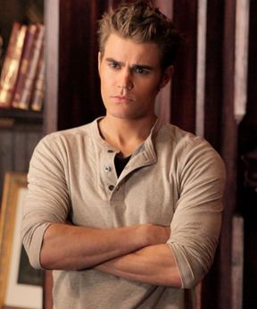 Stefan Salvatore looking something seriously, with folded hands, spiked brown hands , wearing a full slives grey t shirt