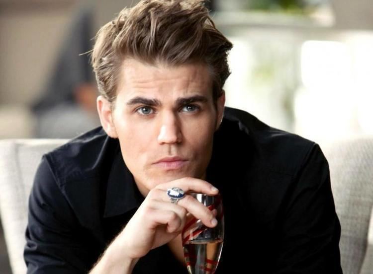 Stefan Salvatore looking something seriously, holding a wine glass with his fingers, ring in his middle finger, spiked brown hairs, wearing a black shirt.
